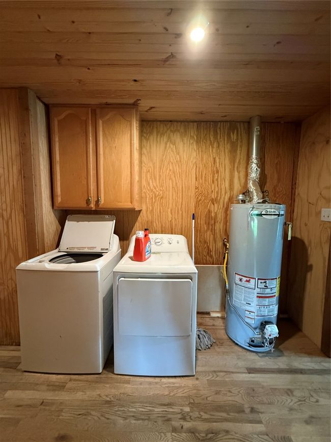 Laundry room with water heater, wooden ceiling, washer and clothes dryer, cabinet space, and light wood-style floors | Image 40
