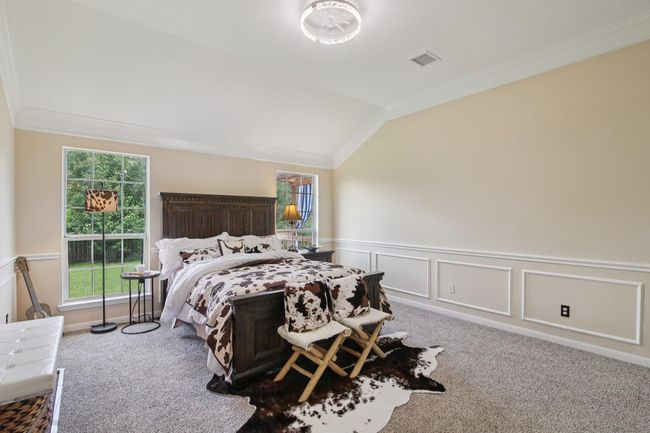 This spacious bedroom features a vaulted ceiling and large windows that provide plenty of natural light. Neutral walls and carpeting offer a cozy and inviting atmosphere. | Image 18