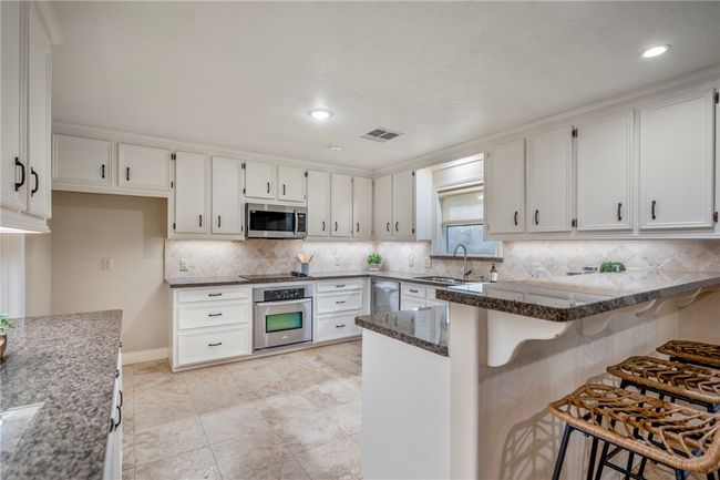 Kitchen with stainless steel appliances, a peninsula, a sink, visible vents, and dark stone counters | Image 14
