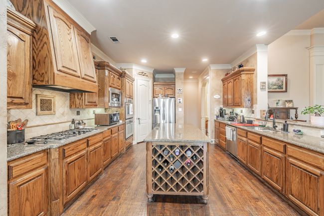 Kitchen featuring appliances with stainless steel finishes, ornamental molding, light stone countertops, dark wood finished floors, and backsplash | Image 20