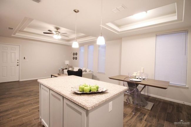 Kitchen featuring a tray ceiling, dark wood finished floors, decorative light fixtures, a center island, and open floor plan | Image 8