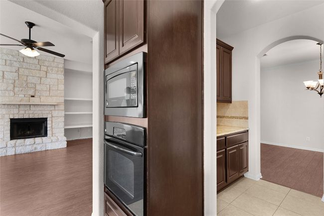 Kitchen with built in microwave, arched walkways, dark brown cabinets, black oven, and ceiling fan with notable chandelier | Image 25