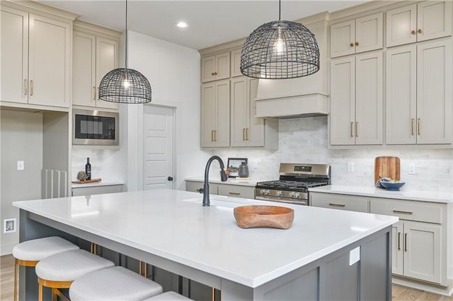 Kitchen featuring black microwave, stainless steel gas stove, light hardwood / wood-style floors, decorative backsplash, and an island with sink | Image 13