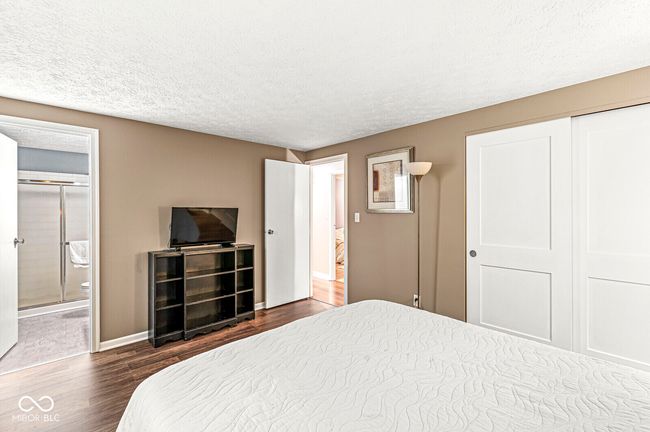 bedroom with dark wood-style flooring, a textured ceiling, connected bathroom, and a closet | Image 13