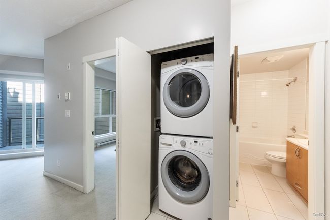 Laundry room featuring stacked washer / drying machine, light tile patterned flooring, light carpet, and a baseboard heating unit | Image 17