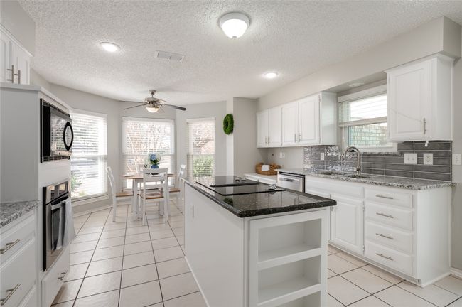 Kitchen featuring black appliances, light tile patterned floors, a sink, and a center island | Image 13