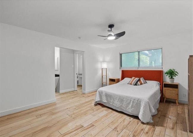 Spacious bedroom (originally the primary suite) with natural wood look flooring, modern fan, and ample light. This room also features a beautiful en-suite bath with standing shower. | Image 34