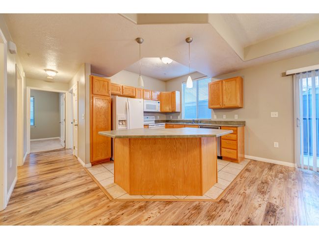 Kitchen with white appliances, light wood-type flooring, a center island, baseboards, and hanging light fixtures | Image 10