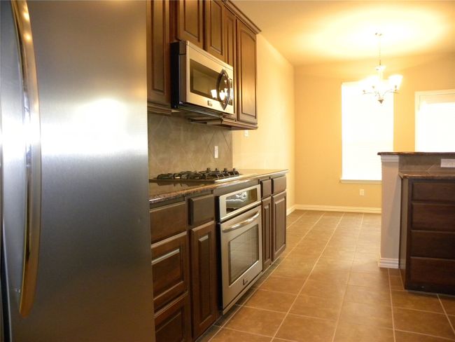 Kitchen with appliances with stainless steel finishes, decorative backsplash, a chandelier, dark tile patterned flooring, and hanging light fixtures | Image 20