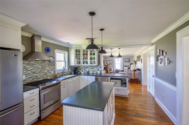 Kitchen featuring appliances with stainless steel finishes, wall chimney range hood, dark countertops, a sink, and tasteful backsplash | Image 12