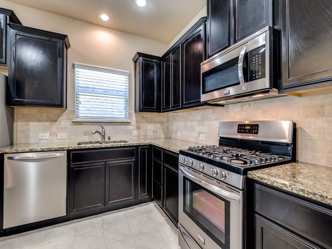 Kitchen with appliances with stainless steel finishes, a sink, light stone countertops, and dark cabinets | Image 6