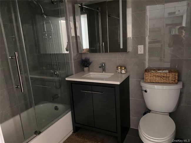 Bathroom with bath / shower combo with glass door, tile walls, vanity, backsplash, and dark tile patterned flooring | Image 12
