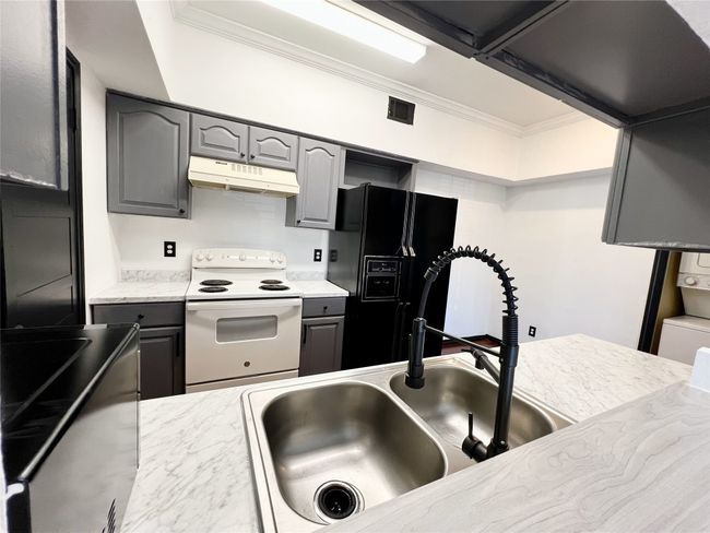 Kitchen featuring black refrigerator with ice dispenser, stacked washer / dryer, under cabinet range hood, white electric range oven, and gray cabinets | Image 7