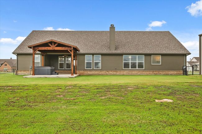 Back of house featuring a hot tub, a patio area, a chimney, and roof with shingles | Image 24