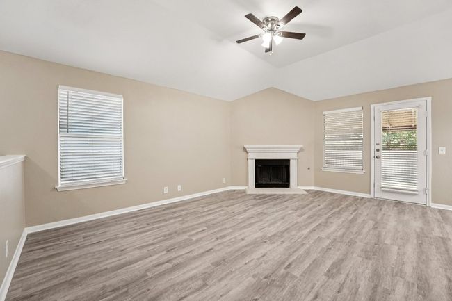 Unfurnished living room featuring a fireplace with raised hearth, light wood-type flooring, a ceiling fan, and lofted ceiling | Image 5