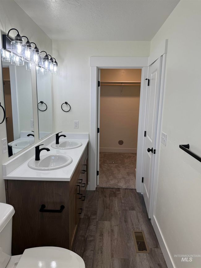 Bathroom featuring wood finished floors, double vanity, a walk in closet, and a textured ceiling | Image 6