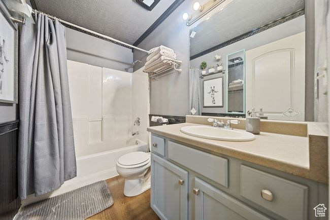 Full bath featuring a textured ceiling, toilet, shower / tub combo, wood finished floors, and vanity | Image 15