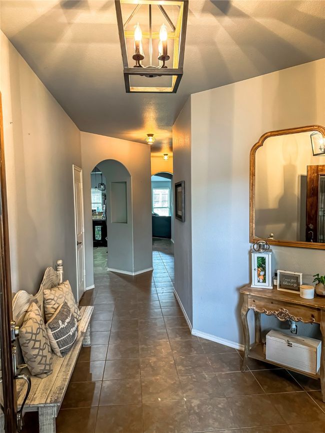 Hall with arched walkways, dark tile patterned floors, a notable chandelier, and baseboards | Image 4