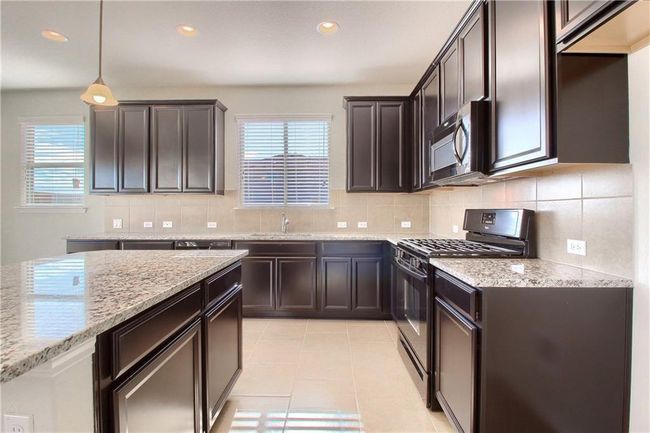 Kitchen featuring black gas stove, stainless steel microwave, a sink, light stone counters, and healthy amount of natural light | Image 8