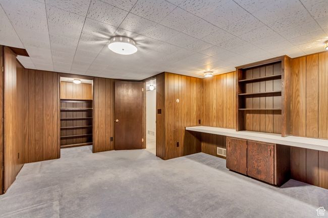 Unfurnished office with visible vents, wood walls, carpet floors, and built in shelves | Image 23
