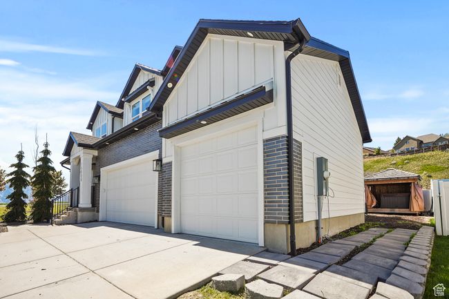 View of side of home with board and batten siding, concrete driveway, brick siding, and a garage | Image 4
