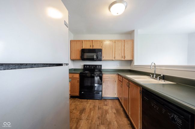 kitchen featuring dark countertops, a sink, black appliances, light brown cabinetry, and dark wood finished floors | Image 14