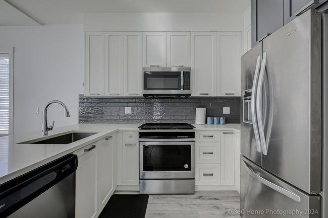 Kitchen with appliances with stainless steel finishes, backsplash, light countertops, and white cabinets | Image 4
