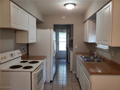 Kitchen featuring white range with electric cooktop, white cabinetry, sink, light tile patterned flooring, and washer / clothes dryer | Image 3