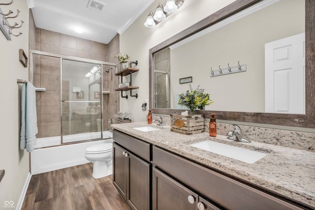 bathroom featuring double vanity, vinyl plank flooring, bath / shower combo with tiled wall, glass door, and crown molding | Image 11