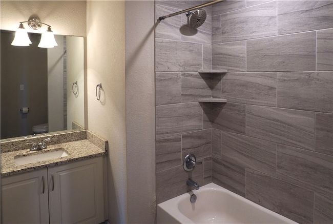 Bathroom with washtub / shower combination, vanity, a textured wall, and toilet | Image 15
