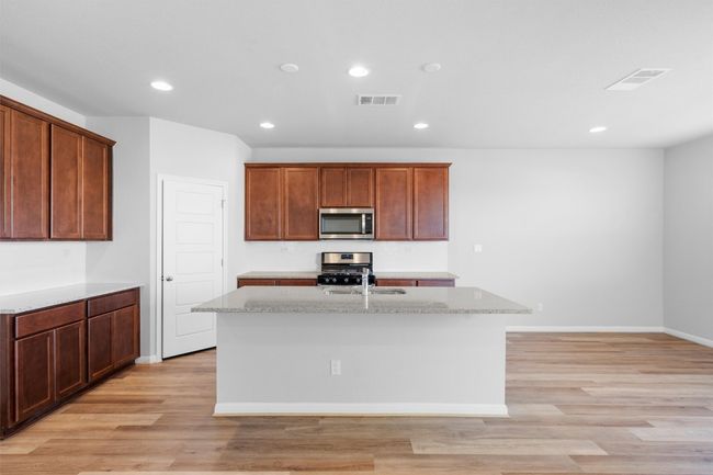 Kitchen with stainless steel appliances, a kitchen island with sink, light wood-style floors, recessed lighting, and light stone countertops | Image 8
