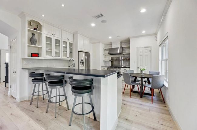 Kitchen with open shelves, stainless steel fridge with ice dispenser, dark countertops, wall chimney range hood, and a peninsula | Image 12