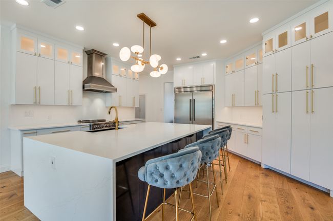 Kitchen featuring light wood-type flooring, recessed lighting, stainless steel built in refrigerator, a sink, and wall chimney exhaust hood | Image 5
