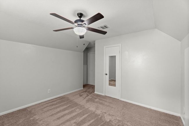 This secondary bedroom features neutral walls and carpet, with a ceiling fan for comfort. It includes a door with a full-length mirror, adding functionality to the space- Ideal for a bedroom or office. | Image 28