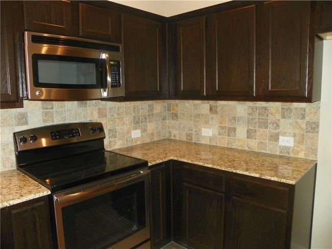 Kitchen featuring appliances with stainless steel finishes, dark brown cabinets, backsplash, and light stone counters | Image 5