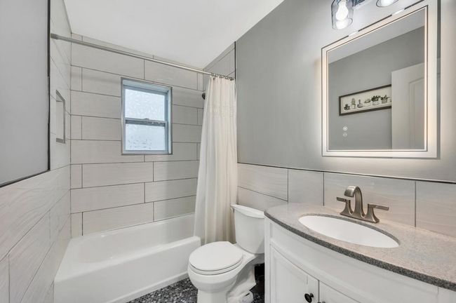 Full bath featuring vanity, tile walls, toilet, decorative backsplash, and shower / bath combo with shower curtain | Image 17
