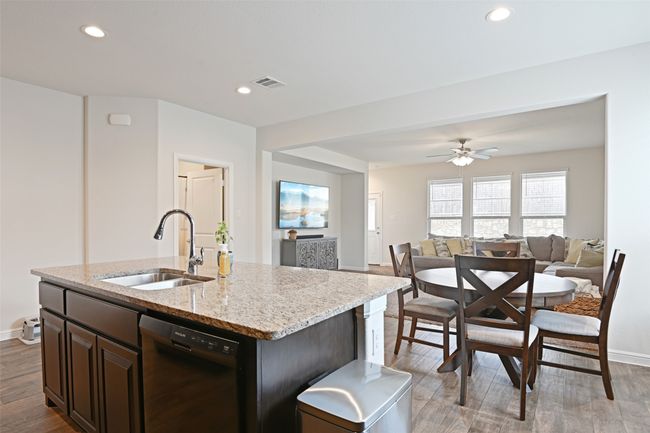 Kitchen featuring black dishwasher, a sink, light wood-style flooring, open floor plan, and light stone countertops | Image 7