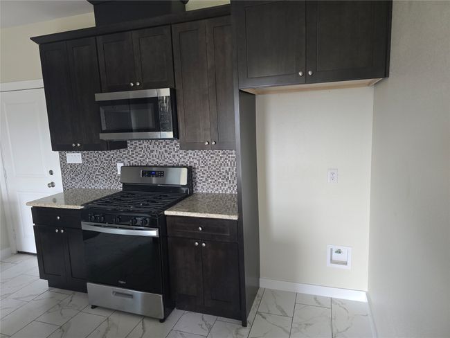 Kitchen with stainless steel appliances, light marble finish flooring, baseboards, backsplash, and light stone counters | Image 8