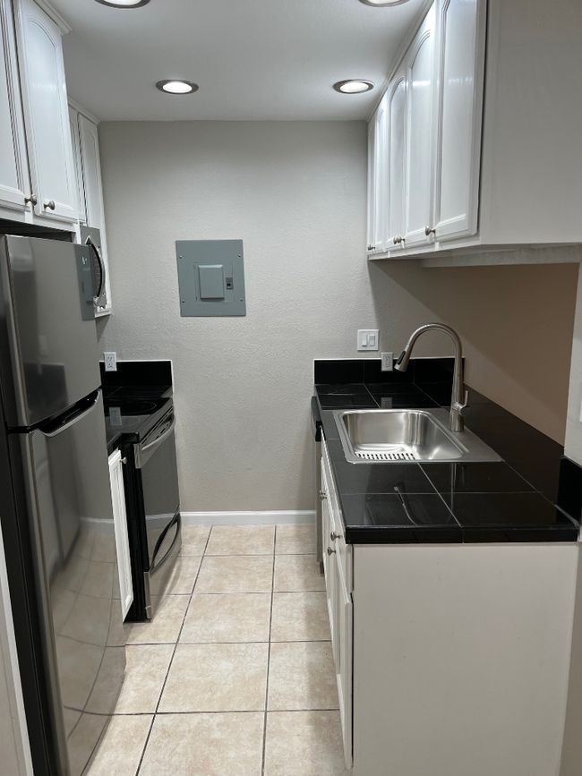 Kitchen featuring stove, a sink, electric panel, fridge, and white cabinetry | Image 6