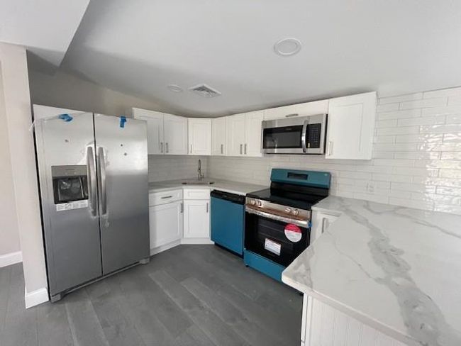 Kitchen with a sink, white cabinets, stainless steel appliances, backsplash, and light stone countertops | Image 4