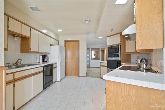 Kitchen featuring black appliances, tasteful backsplash, wall chimney exhaust hood, and light tile patterned floors | Image 7