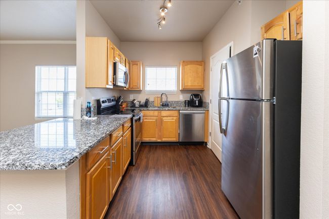 kitchen with dark stone countertops, a peninsula, vinyl plank floors, appliances with stainless steel finishes, and a sink | Image 9
