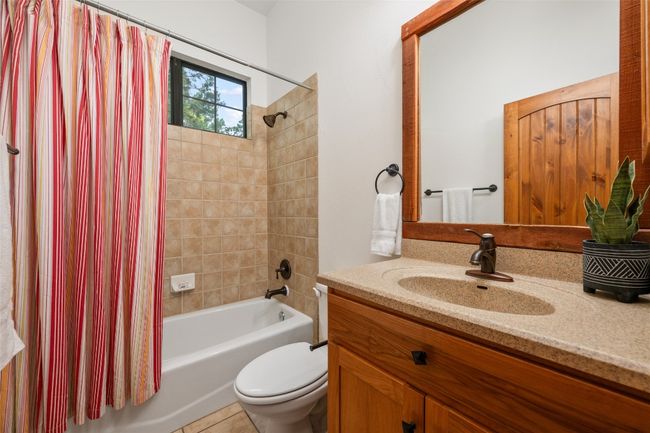 This secondary bath features a tiled shower and bathtub, a natural wood vanity with solid surface counter, oil rubbed bronze fixtures, and a framed mirror. | Image 18