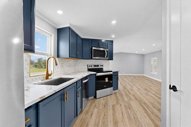 Kitchen featuring appliances with stainless steel finishes, a sink, blue cabinetry, light wood-style flooring, gold faucets matching with cabinet handles and luxury back splash. | Image 17