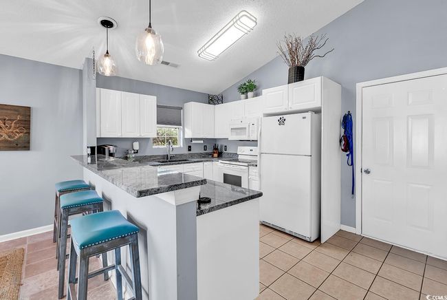 Kitchen with white appliances, lofted ceiling, a breakfast bar area, a peninsula, and dark stone counters | Image 18