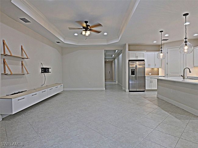 Unfurnished living room with a raised ceiling, a ceiling fan, crown molding, light tile patterned floors, and recessed lighting | Image 6