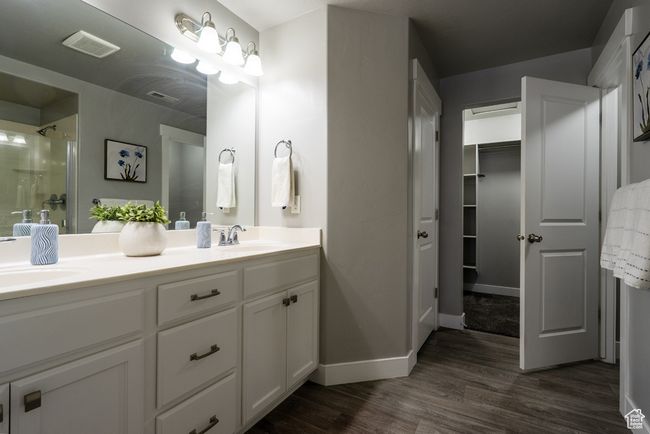 Bathroom featuring double vanity, wood finished floors, an enclosed shower, baseboards, and a walk in closet | Image 10