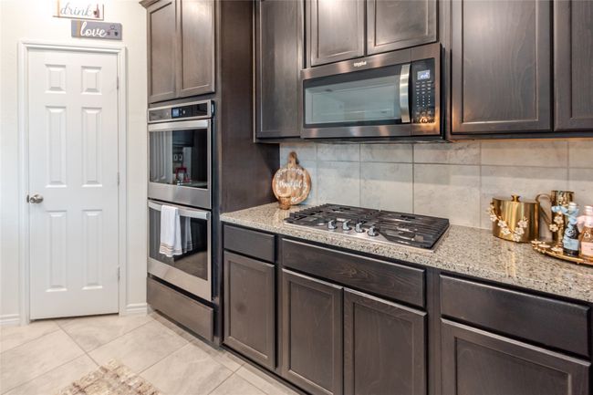 Kitchen featuring appliances with stainless steel finishes, dark brown cabinets, light tile patterned floors, and backsplash | Image 5