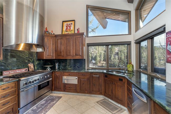 Kitchen with appliances with stainless steel finishes, wall chimney exhaust hood, dark stone counters, decorative backsplash, and sink | Image 15