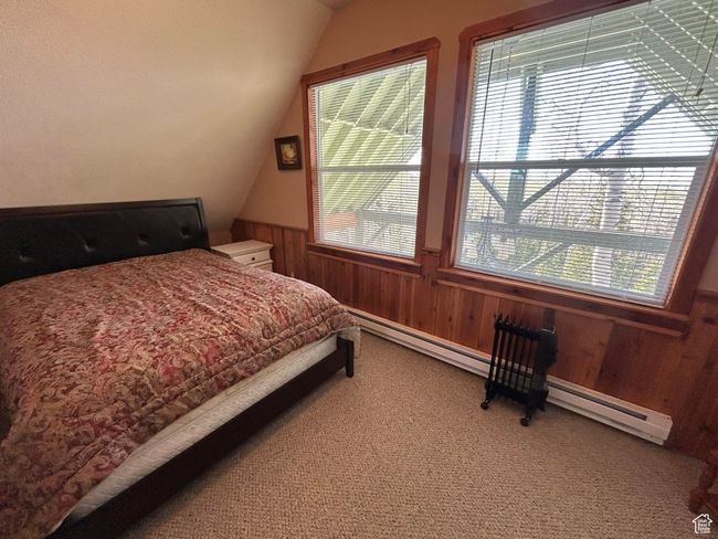 Bedroom with light carpet, vaulted ceiling, a baseboard radiator, wainscoting, and wood walls | Image 30